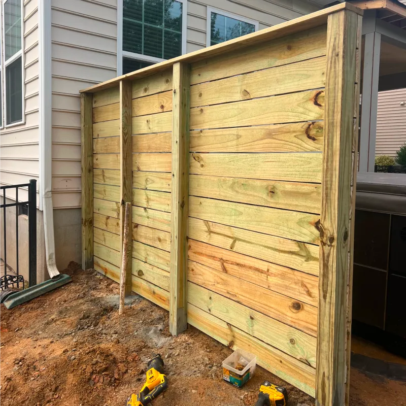 A new wooden privacy fence partially built in a backyard with construction tools on the dirt ground.